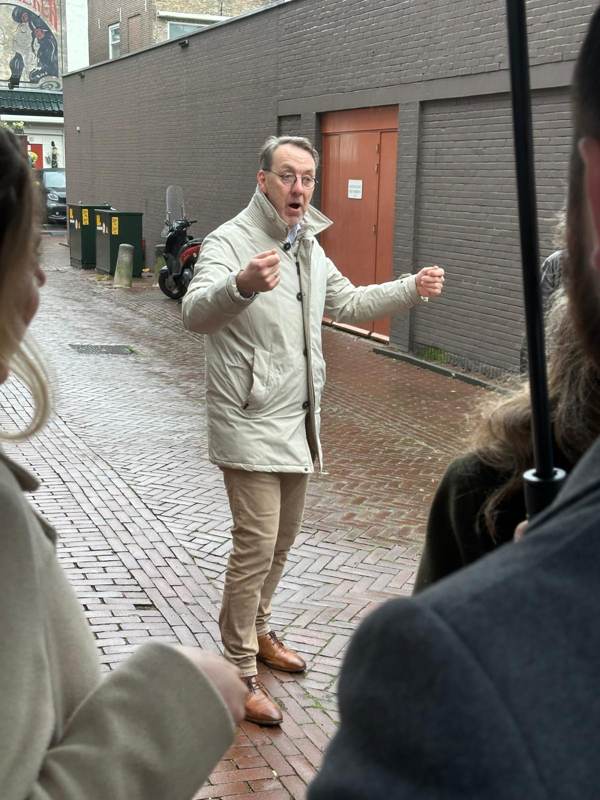 De gids in een lichte jas vertelt met beide handen in de lucht