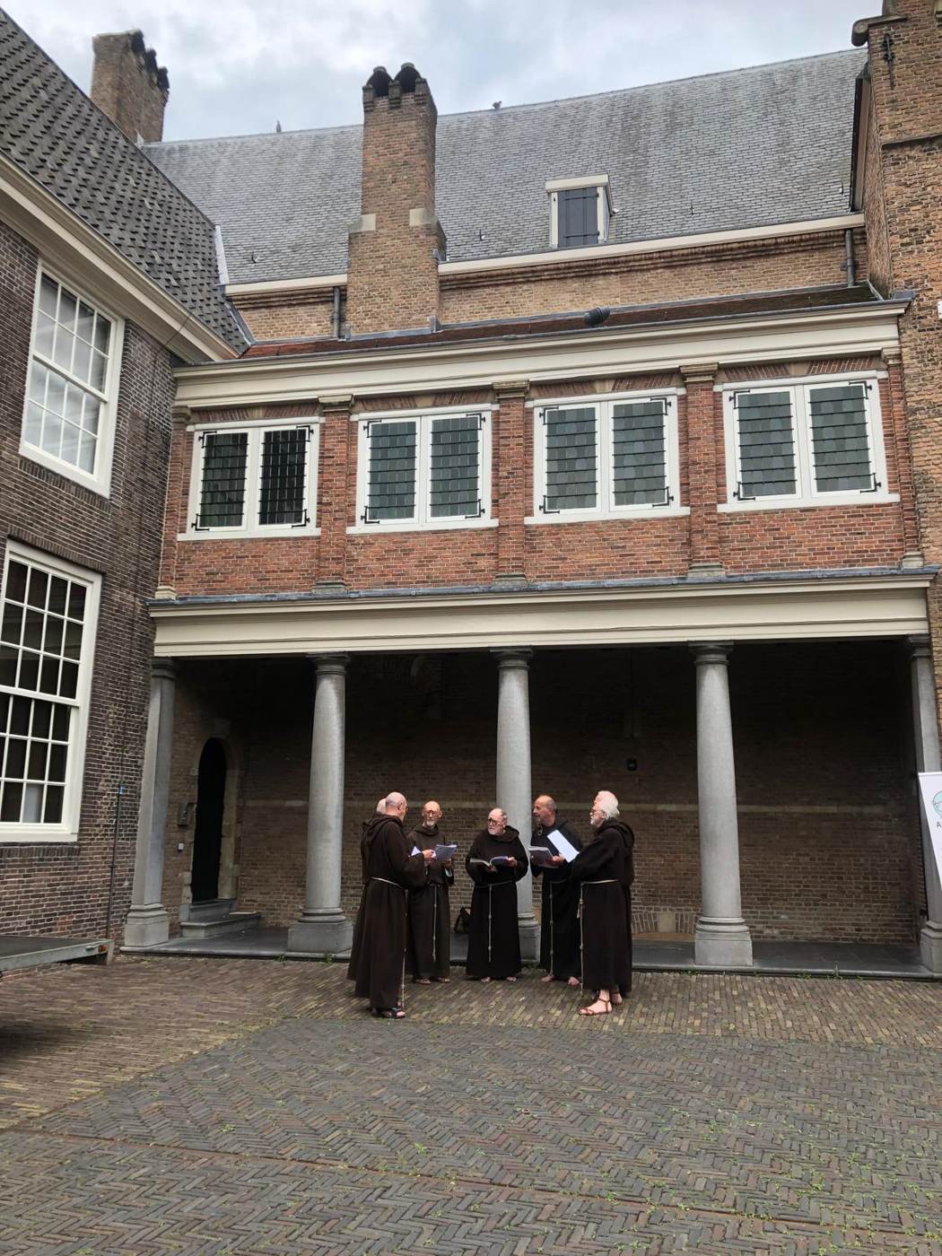 Een binnenplaats met zuilengang, waar vier mensen in monnikspij staan