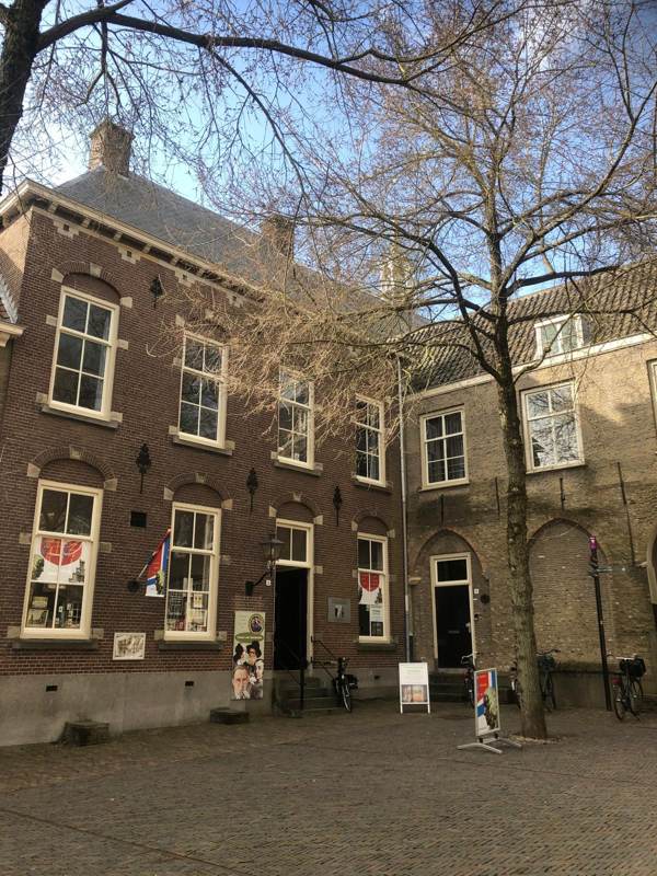 Een plein met een kale boom voor een bakstenen gebouw met luiken
