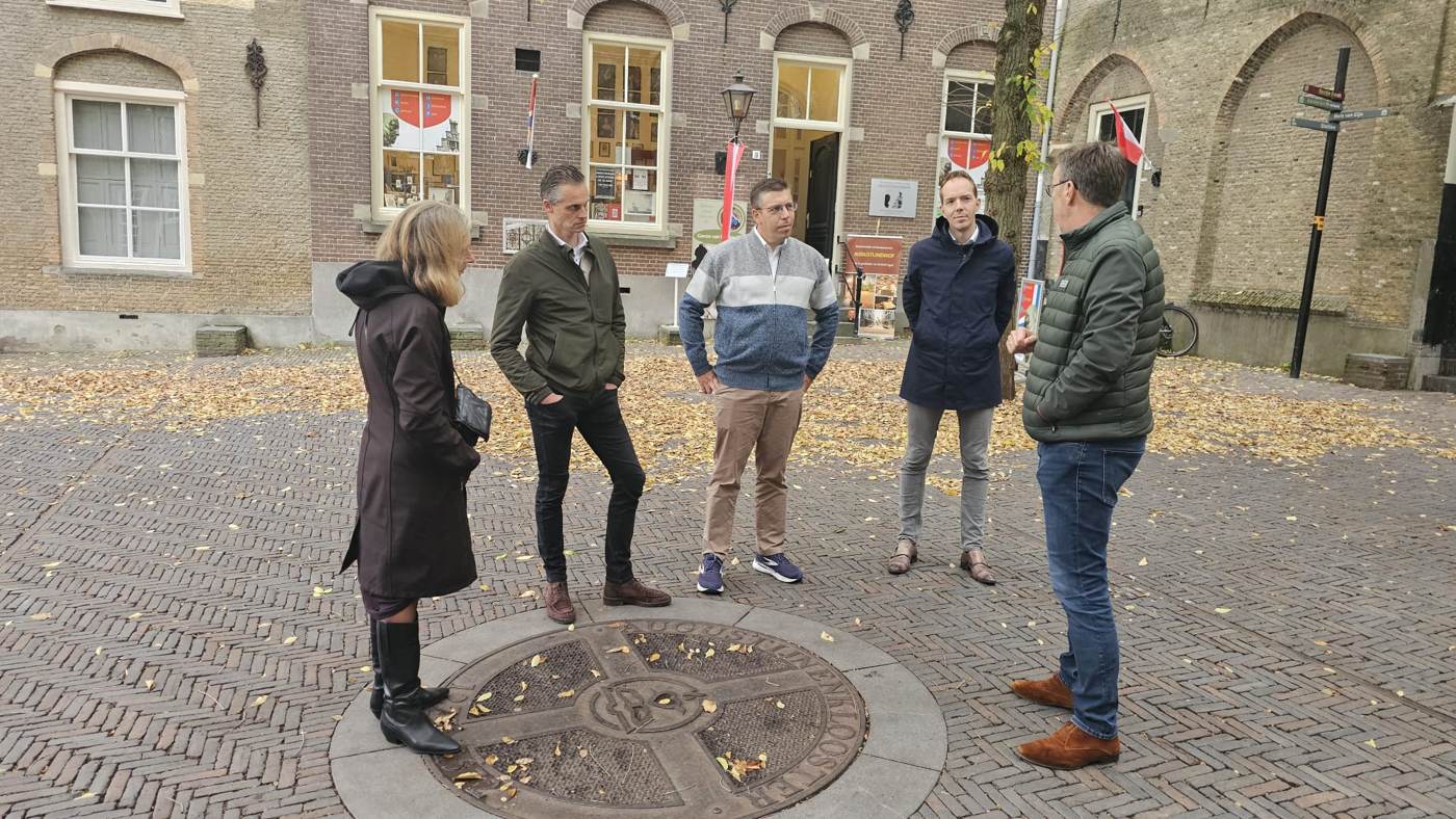 Een kleine groep luistert op een plein met een stenen medaillon in de bestrating